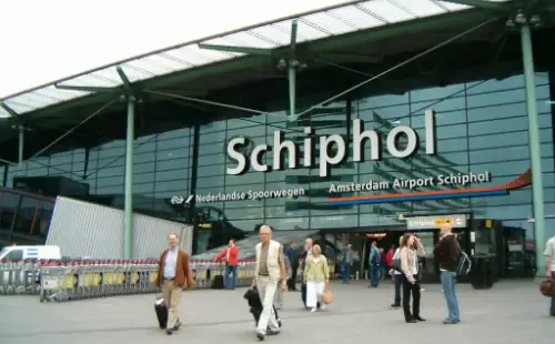 Reizigers met koffers voor de ingang van Schiphol Plaza en het NS-station